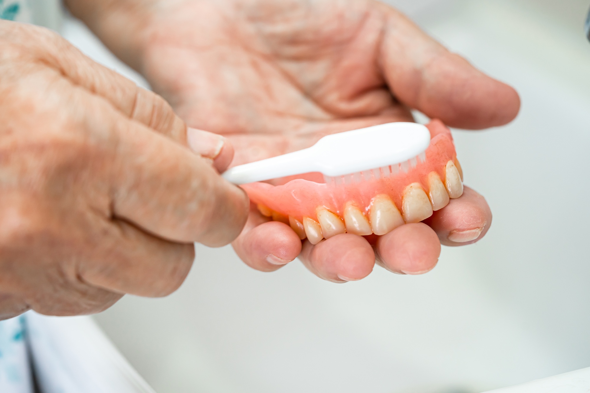 Asian senior or elderly old woman patient use toothbrush to clean partial denture of replacement